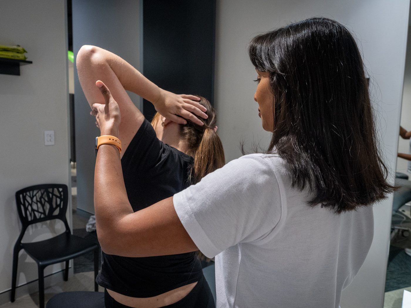 A physiotherapist guiding a patient's raised arm through a shoulder and upper back stretch